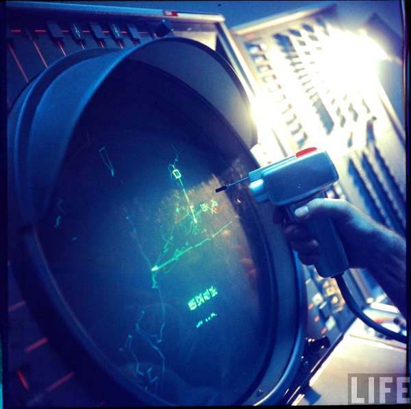 A SAGE operator uses a light gun on the console display, tracking symbols on the scope